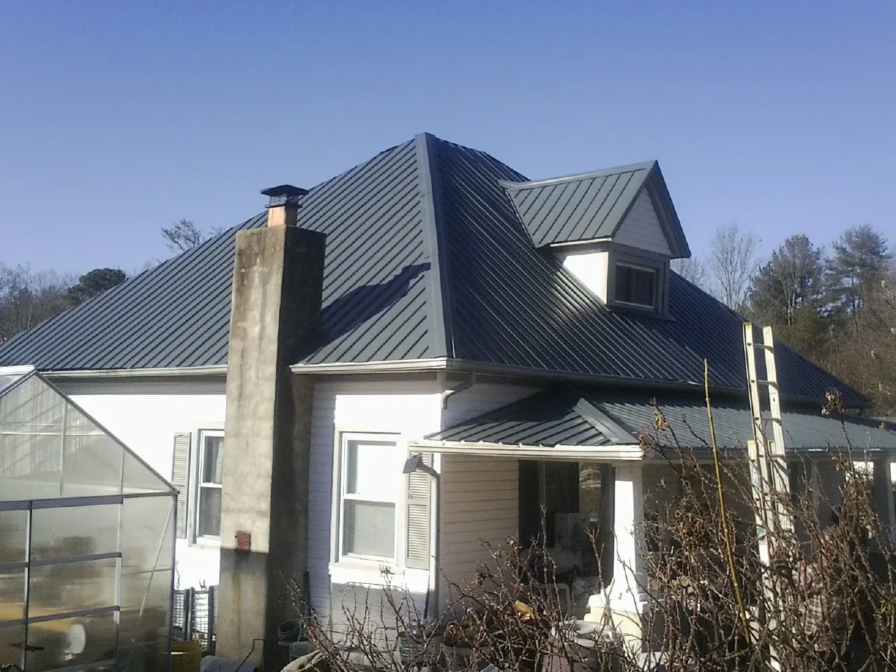Dark blue standing seam metal roof on a white farmhouse with dormer — Slate & Tile Roof Repair by Roofing Brothers in Crozet