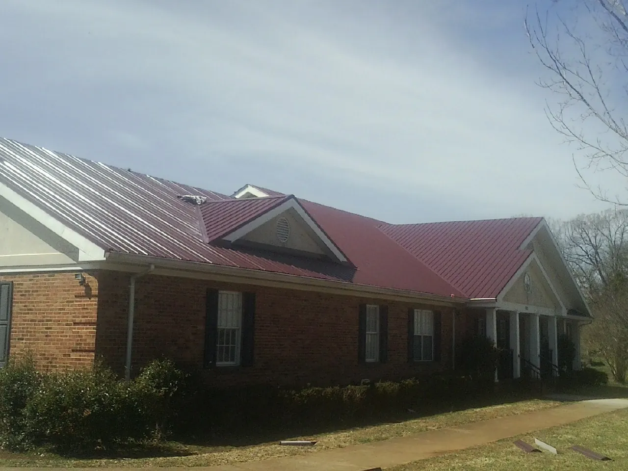 Red metal roof with gabled entries on a long brick building, from a Hail Damage Roof Repair job in Crozet