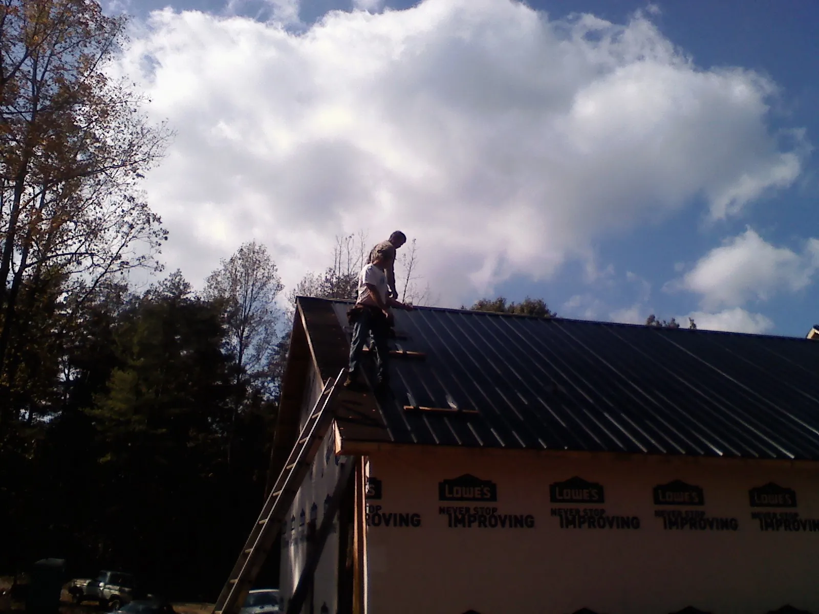 Roofer fastening dark metal panels high against a cloudy sky, from a Roof Inspection job in Crozet